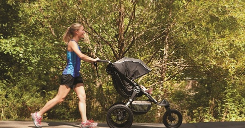 A woman jogs in the park while pushing a stroller.