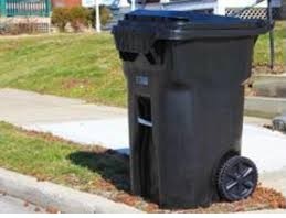 A black garbage can sitting on a curb.